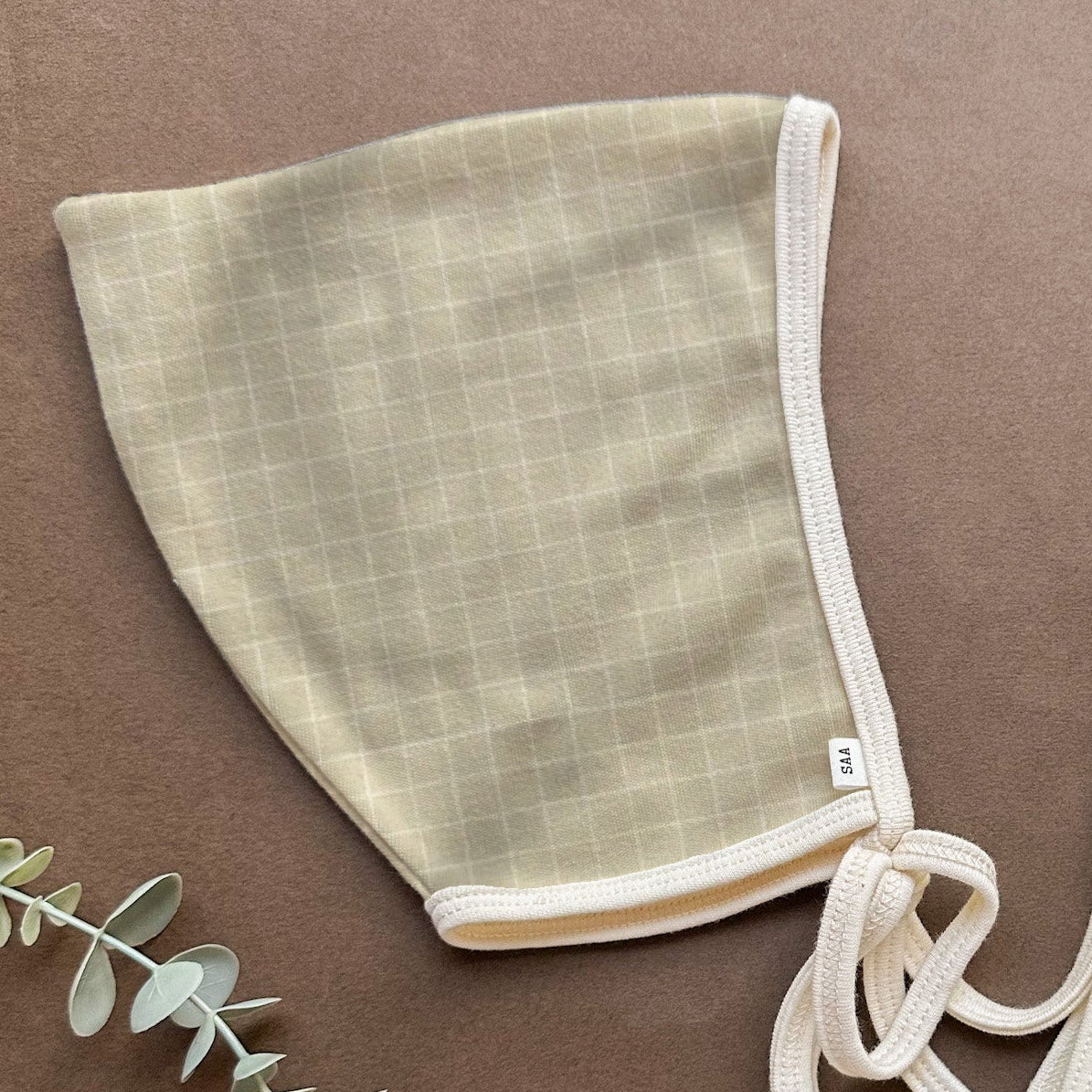 Textured green cotton baby bonnet with white trim on a brown background.