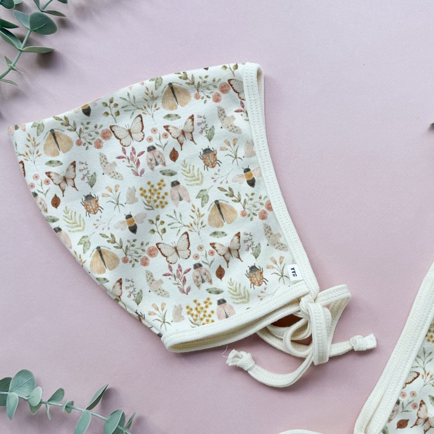 Floral-patterned cotton baby bonnet on a pink background.