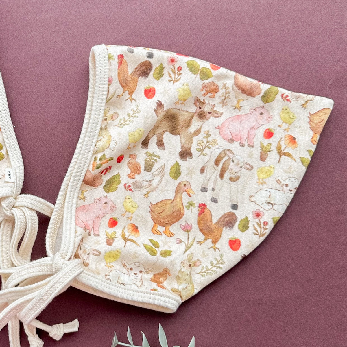 A cotton baby bonnet with animal pattern on a purple background.