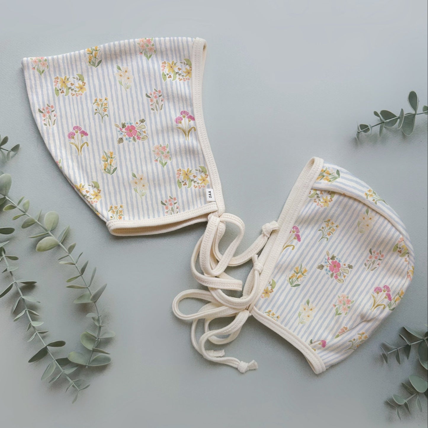 Two floral-patterned baby hats on a light gray background with green leaves.