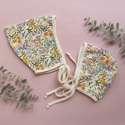 Floral-patterned baby bonnet on a pink background with green leaves.