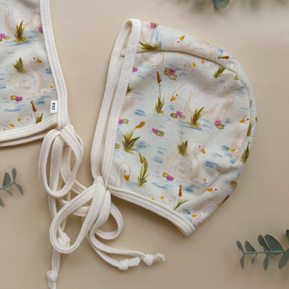 Baby bonnet with swan pattern on a beige background