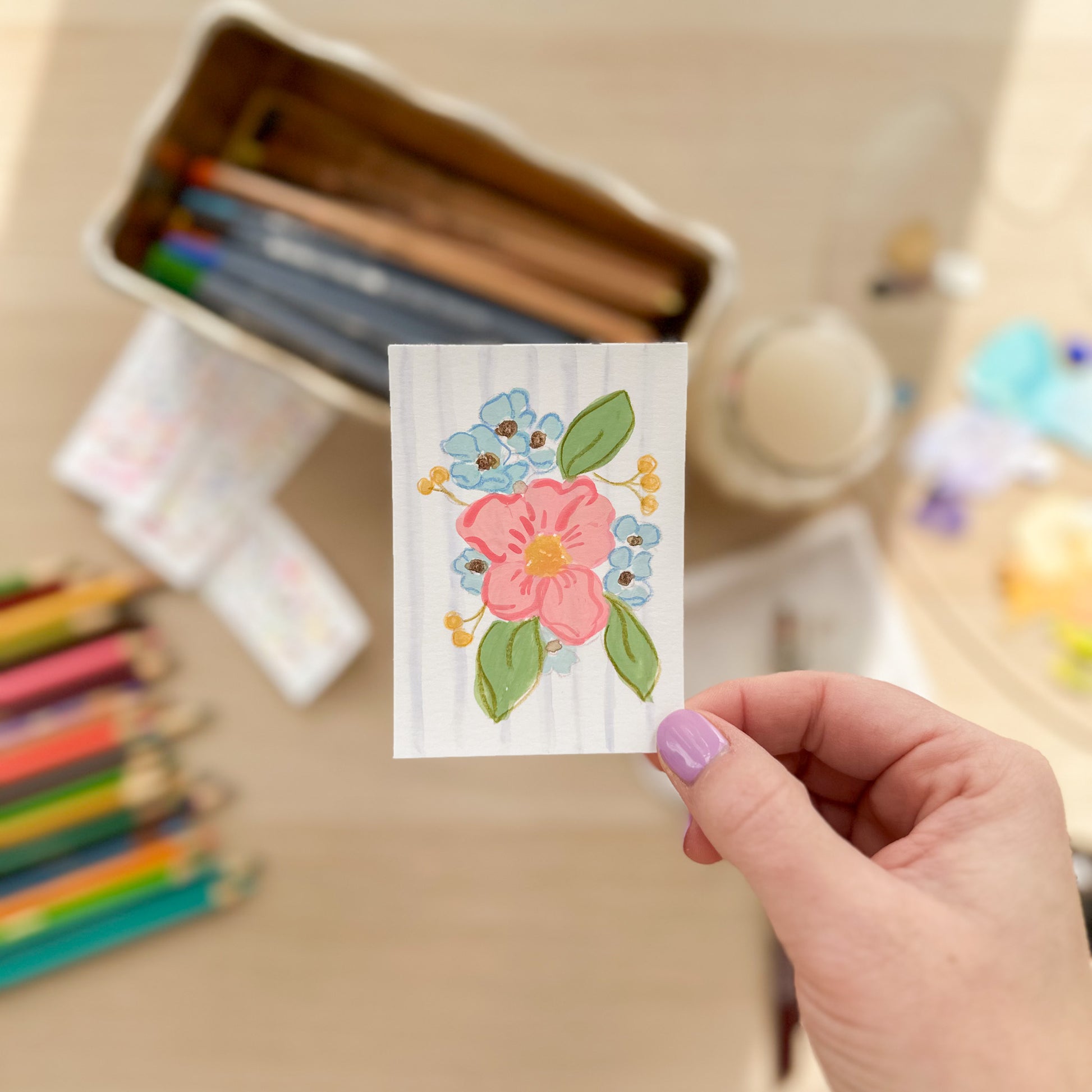 Hand holding a card with floral design in a craft setting. ACEO original artwork by Carrie Keefe - Bloom by April