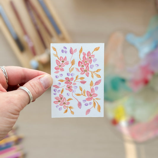 Hand holding a small card with floral design in front of colorful pencils. ACEO original artwork by Carrie Keefe - Bloom by April