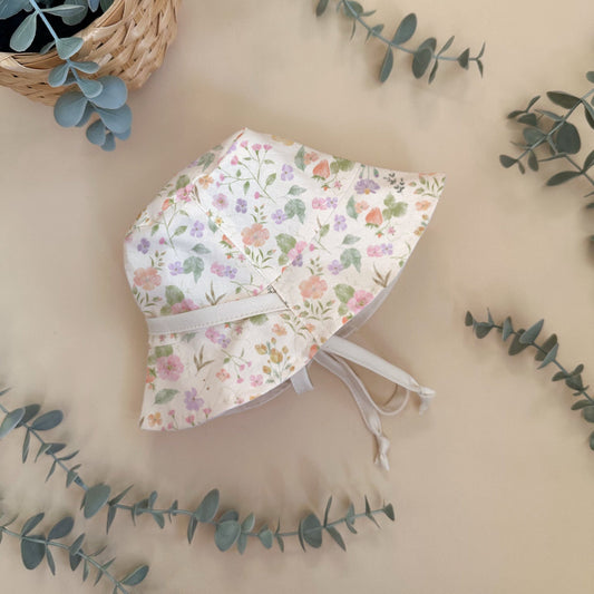 Floral baby bonnet on a beige background with greenery