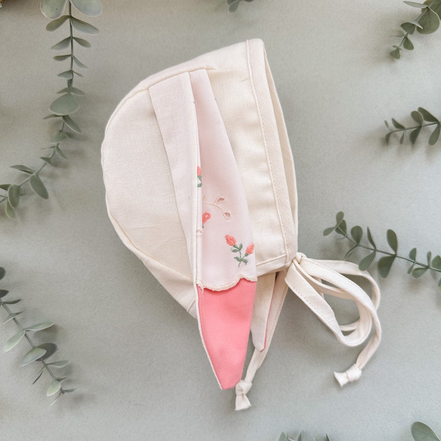 Baby bunny bonnet with floral pattern on a light gray background with green leaves.