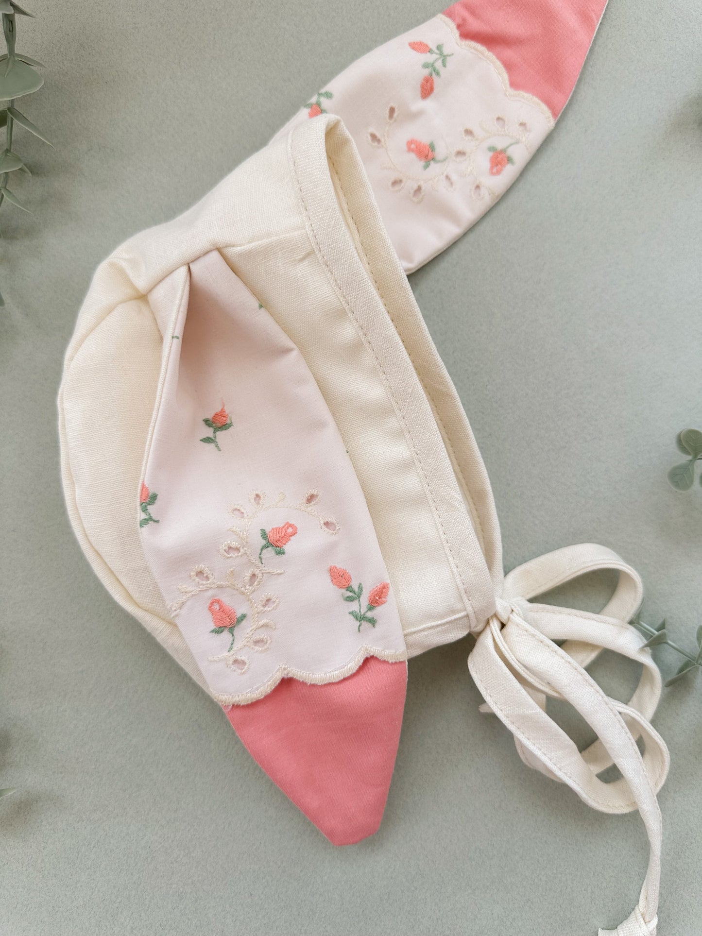 Baby bonnet with floral embroidery on a light green background