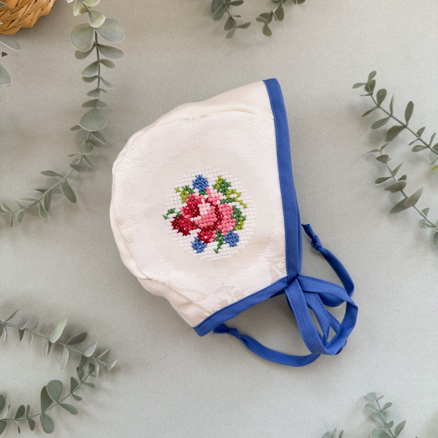Baby bonnet with floral embroidery on a light background with greenery