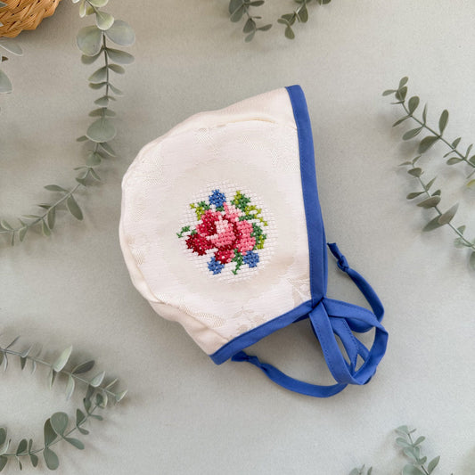 Baby bonnet with floral embroidery on a light background with greenery