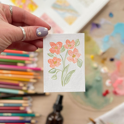 Hand holding a small card with floral design in a colorful setting. ACEO original artwork by Carrie Keefe - Bloom by April