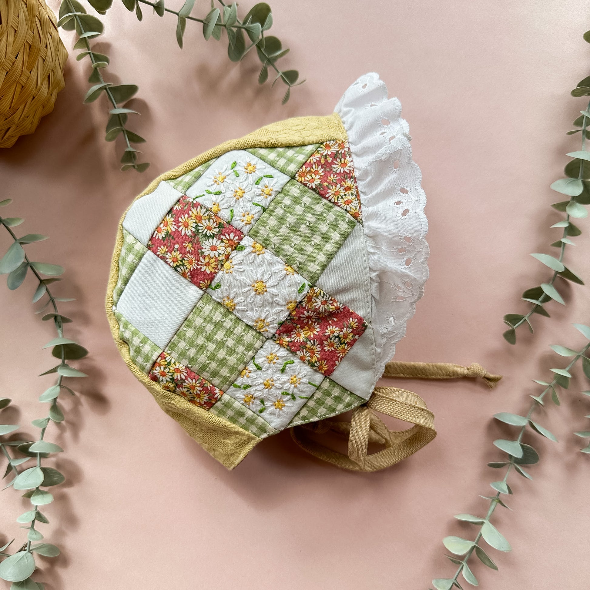 Patchwork bonnet with floral and green patterns on a pink background with eucalyptus leaves.