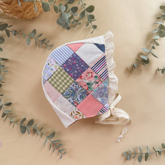 Patchwork baby bonnet on a beige background with green leaves