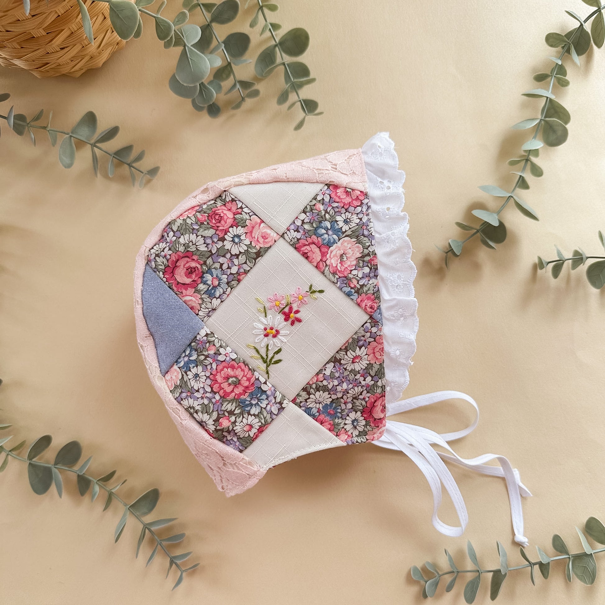 Floral patchwork baby bonnet on a beige background with green leaves