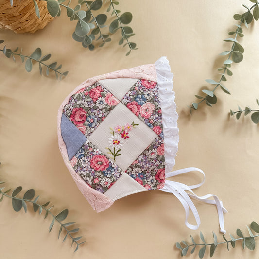 Floral patchwork baby bonnet on a beige background with green leaves
