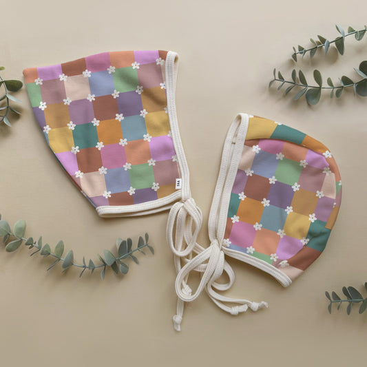 Colorful checkered baby bonnets on a beige background with green leaves.
