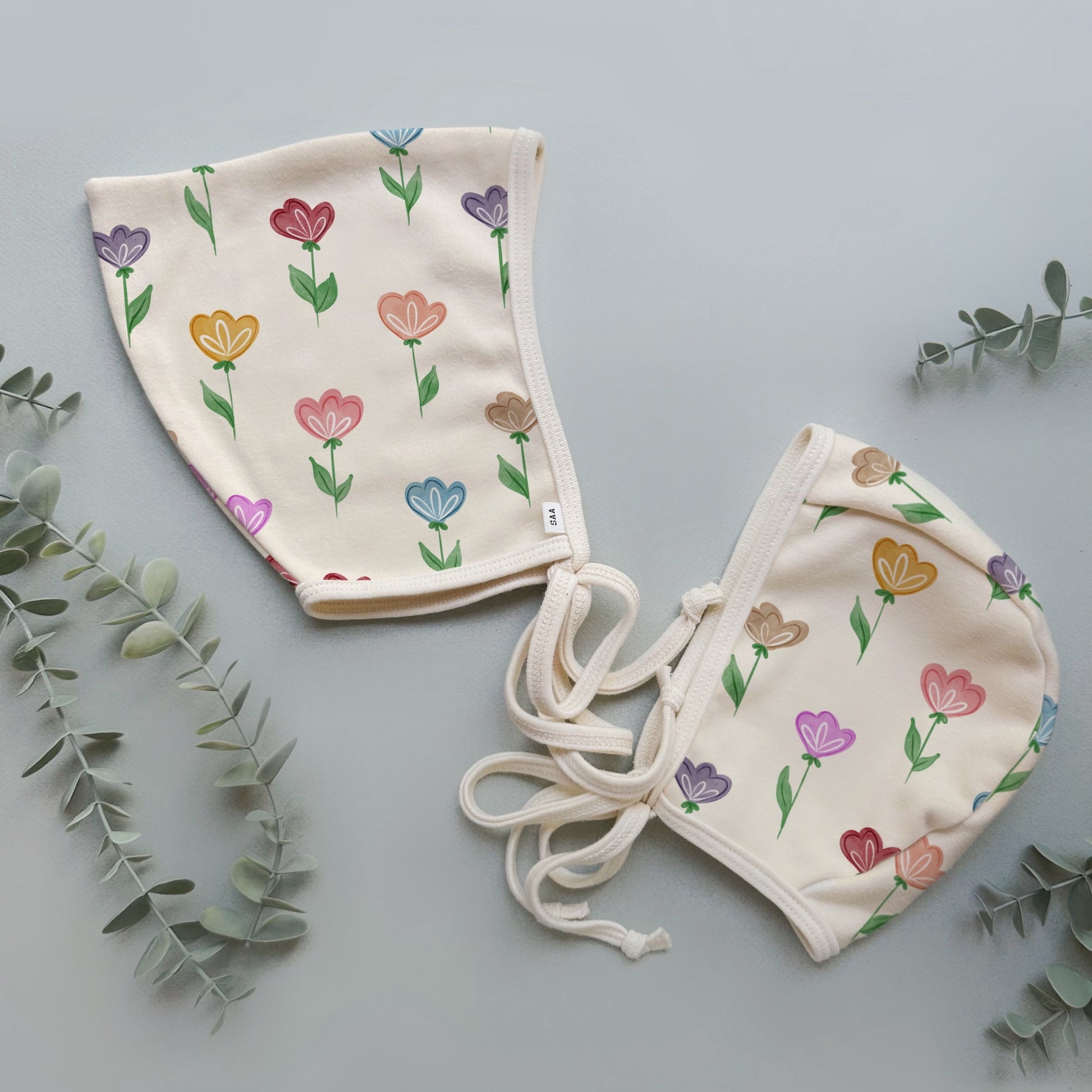 Two baby bonnets with floral patterns on a light gray background