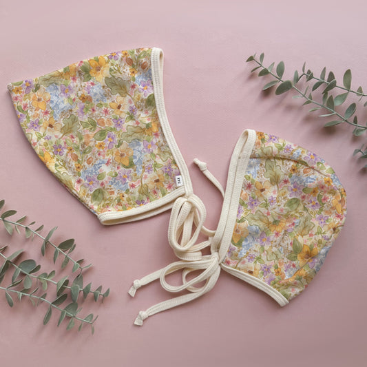 Floral-patterned baby bonnet on a pink background with green leaves.