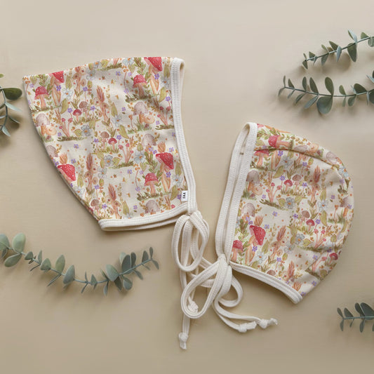 Mushroom floral-patterned baby bonnets on a beige background with green leaves.