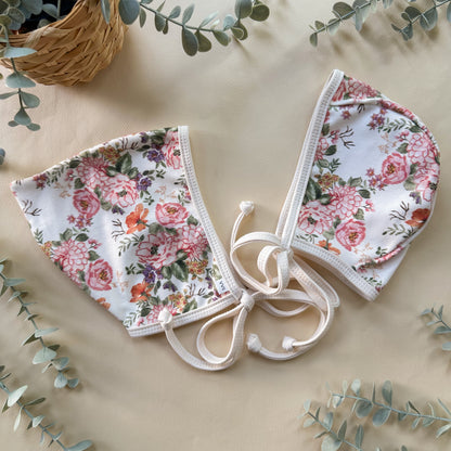 Floral-patterned baby hats on a beige surface with green leaves.