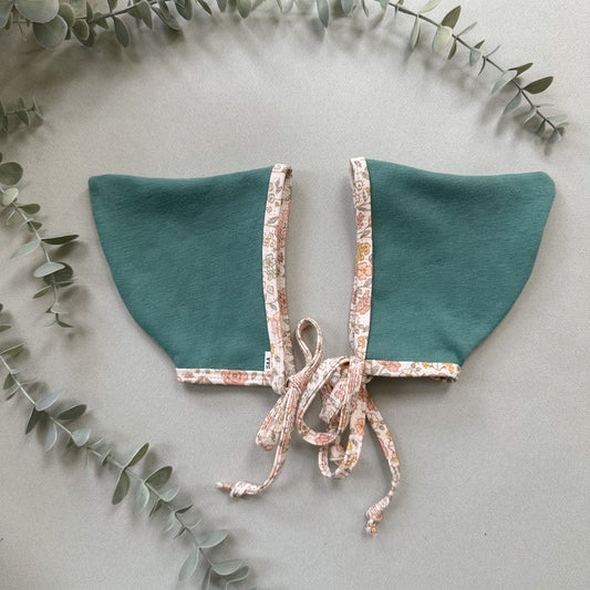 Teal fabric collar with floral trim on a light background with eucalyptus leaves.