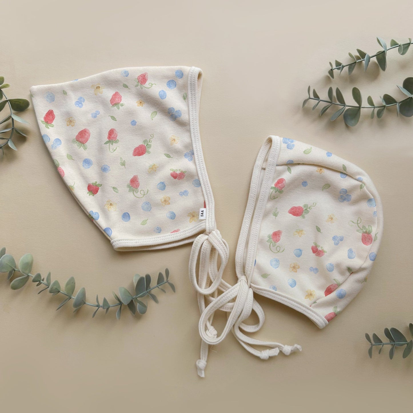 Two baby bonnets with floral pattern on a beige background