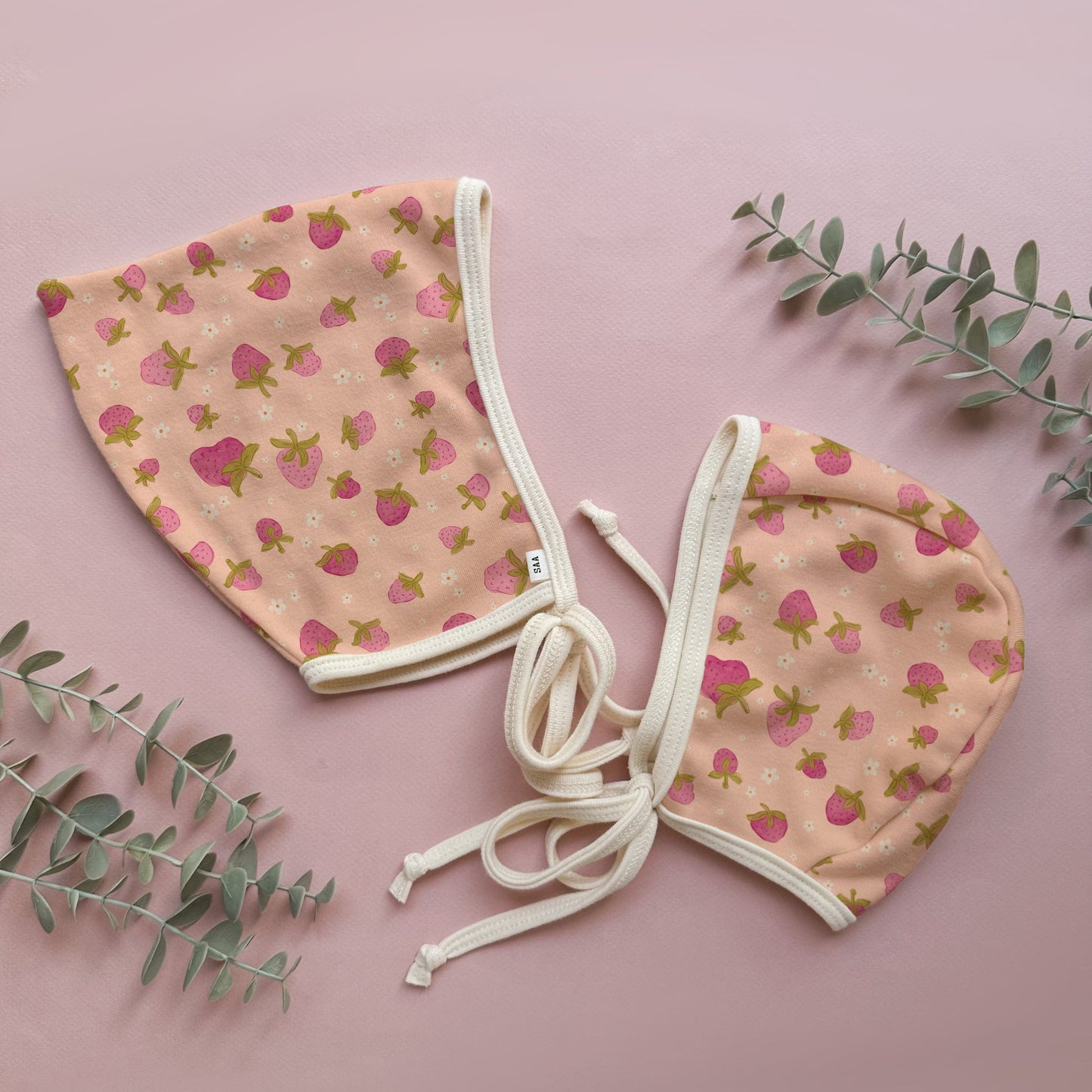 Two baby bonnets with strawberry pattern on a pink background