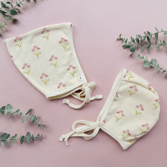 Floral-patterned baby bonnet on a pink background with eucalyptus leaves.