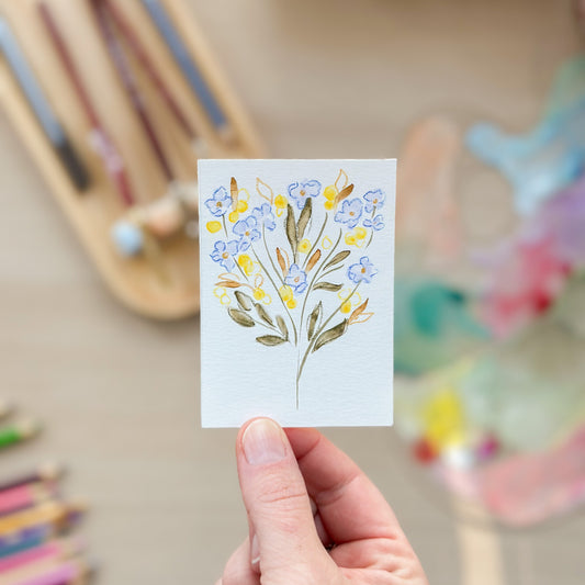 Hand holding a card with a floral design in front of colorful pencils. ACEO original artwork by Carrie Keefe - Bloom by April