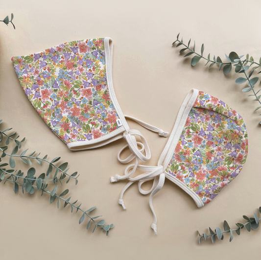 Floral-patterned baby bonnets on a beige background with green leaves.