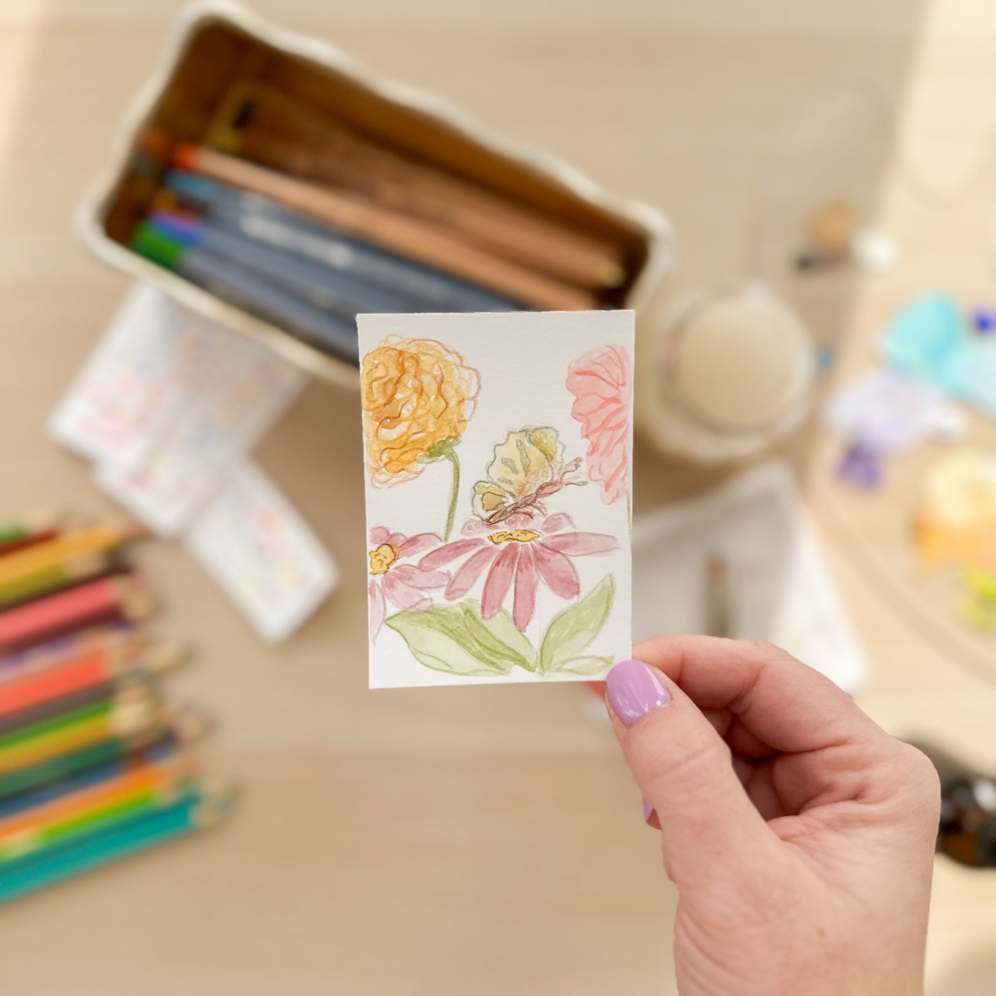 Hand holding a card with floral design in an art studio setting. ACEO original artwork by Carrie Keefe - Bloom by April